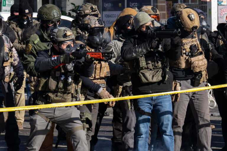 ICE and Border Patrol agents in tactical gear and gas masks stand on Nicollet Avenue in Minneapolis.